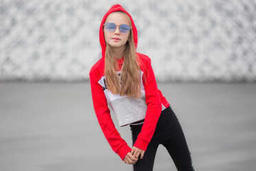 Portrait of a girl in a hood in a suit for dancing. Girl dancing hip hop on the street. Young urban...