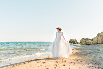 Fototapeta na wymiar Beautiful bride in luxury wedding dress with bouquet at the sea side. Wedding by the sea. Bride walking around the sea near the place of the wedding ceremony.