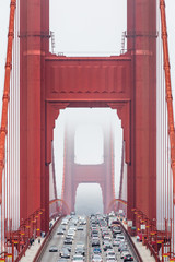Symmetrical front view of the Golden Gate bridge in a foggy day, with traffic flowing on its lanes