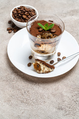Portion of Classic tiramisu dessert in a glass cup on concrete background