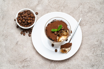 Portion of Classic tiramisu dessert in a glass cup on concrete background