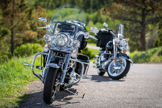 Close up of two motorbikes with chrome details against a background green with trees and meadows