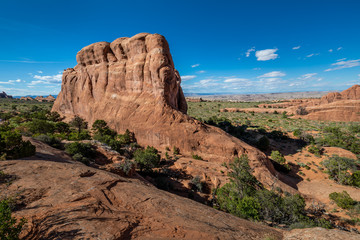 Fototapeta premium Wide angle view of a large red sandstone monolith in Arches National Park, under a blue sky with sparse clouds