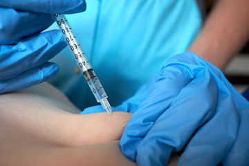 Hands of nurse in blue surgical gloves making injection of anticoagulant subcutaneously to child....