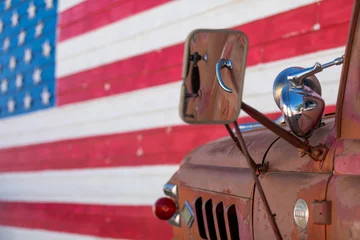 Gordijnen Close up of an old and rusty pickup truck againsta a huge american flag painted on a wall © Roberto