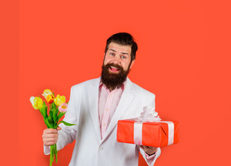 Handsome young man holding gift box and flowers. Businessman with gift and bouquet of tulips for birthday. Romantic man. Bearded man holds bouquet of flowers and gift box. Valentines Day, Womens Day.