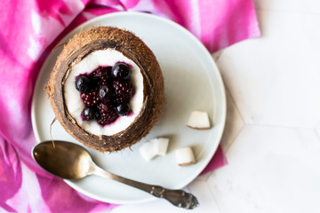 Berry dessert with yogurt in a cup of coconut on a light background. Blackberries, raspberries, blueberries, black currants. Pink napkin