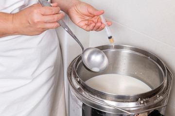 Cheesemaker pours the rennet with a syringe