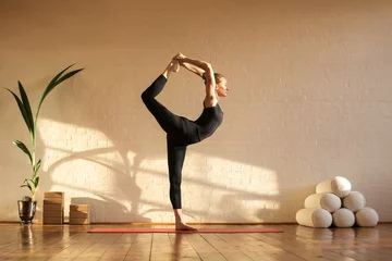 Fotobehang Yogaschool Mooie vrouw die yoga doet bij zonsondergang in een studio