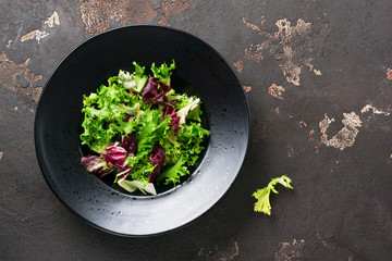 Mix fresh leaves of arugula, lettuce, spinach, beets for salad on a dark stone background....