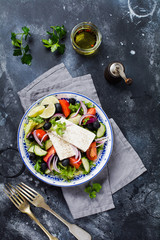 Traditional Greek Salad. Vegetarian dish with fresh lettuce, olives, peppers, cucumbers, onions and feta cheese. On dark rustic concrete background. Top view.