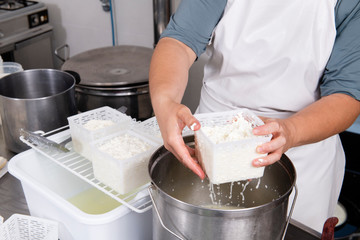 Cheesemaker pours the curdled milk into the plastic forms