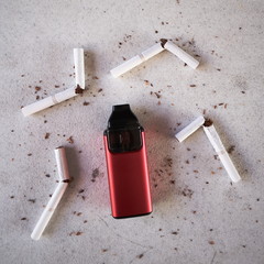 Single red vape electronic cigarette as smoking alternative with broken cigarettes and scattered tobacco on white textured background isolated