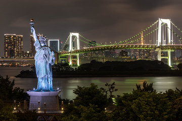 Tokyo skyline at night as seen from Odaiba, with a suspension bridge a statue of liberty replica © Roberto