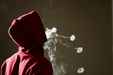 Young male in red hoodie vaping smoking, blows 4 smoke rings, isolated rear view