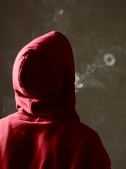 Young male in red hoodie vaping smoking, blows a single smoke ring, isolated rear view