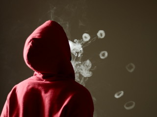 Young male in red hoodie vaping smoking, blows many smoke rings, isolated rear view