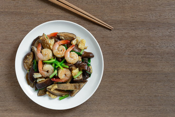 stir fried shiitake mushroom and shrimp with soy sauce in a ceramic dish on wooden table, top view. homemade style food concept.