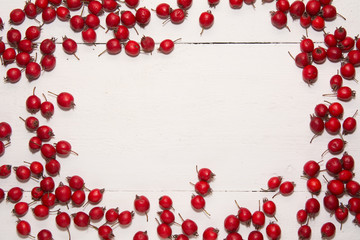 red berries of hawthorn with green leaves white wooden texture background top view frame from berries texture tree