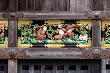 Symmetrical close up shot of a porcelain bas-relief portraing the three wise monkeys framed by a weathered wooden structure