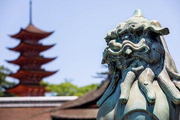 Close up of a bronze statue of a japanese lion, with a red pagod ain the background