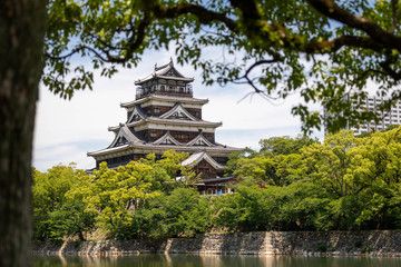 Obraz premium Japanese citycape with a vegetation and a canal in foreground, and an ancient pagoda, emerging from the trees, in the background