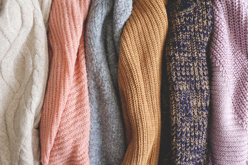 Bunch of knitted warm pastel color sweaters with different vertical knitting patterns hanging in bunch, clearly visible texture. Stylish fall / winter season knitwear clothing. Close up, copy space.