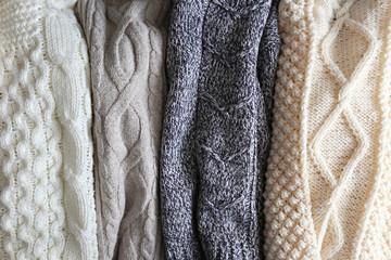 Fototapeta na wymiar Bunch of knitted warm pastel color sweaters with different vertical knitting patterns hanging in bunch, clearly visible texture. Stylish fall / winter season knitwear clothing. Close up, copy space.