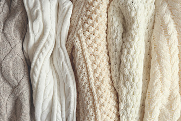 Bunch of knitted warm pastel color sweaters with different vertical knitting patterns hanging in bunch, clearly visible texture. Stylish fall / winter season knitwear clothing. Close up, copy space. - obrazy, fototapety, plakaty