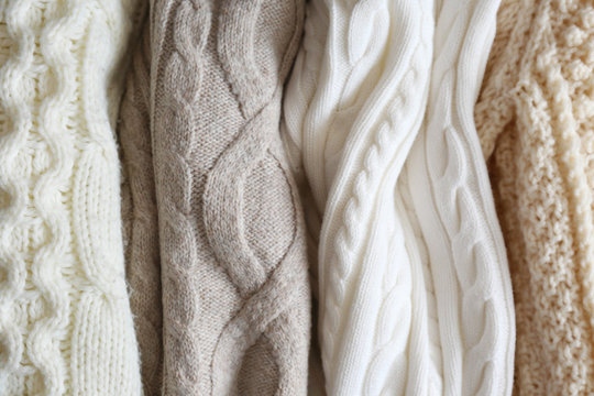 Bunch of knitted warm pastel color sweaters with different vertical knitting patterns hanging in bunch, clearly visible texture. Stylish fall / winter season knitwear clothing. Close up, copy space.
