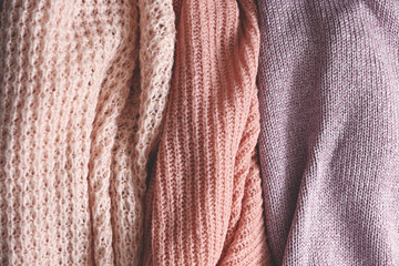 Bunch of knitted warm pastel color sweaters with different vertical knitting patterns hanging in bunch, clearly visible texture. Stylish fall / winter season knitwear clothing. Close up, copy space.