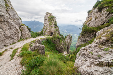 Wide angle shot of an italian mountain landscape, with a trail snaking among rocks in the foreground, and the entrance to a gallery carved into the rock in the background