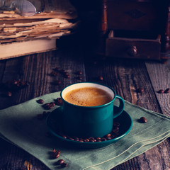 Cafe background with a green cup of espresso coffee standing on a linen napkin with a retro coffee grinder old book. Retro style Nashville. Tonted image. Square image.