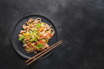 Udon stir-fry noodles with pork bowl and vegetables on black stone background. Asian cuisine. Top...
