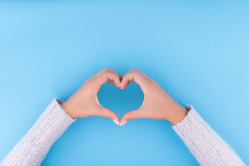 Beautiful woman is hands with a perfect manicure making the heart on blue background. Flat lay...