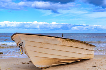 Lonely boat lying on the sand beach at the coast of the island usedom, Germany, under a blue and cloudy sky.