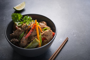 Udon stir-fry noodles with pork bowl and chopsticks on black stone background. Asian cuisine.