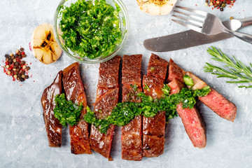Sliced rib eye beef steak with chimichurri sauce and spices on white paper. Striploin cooked on the...