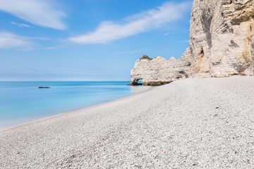 The white rocky beach of Etretat in a bright summer day, under a blue sky with puffy clouds