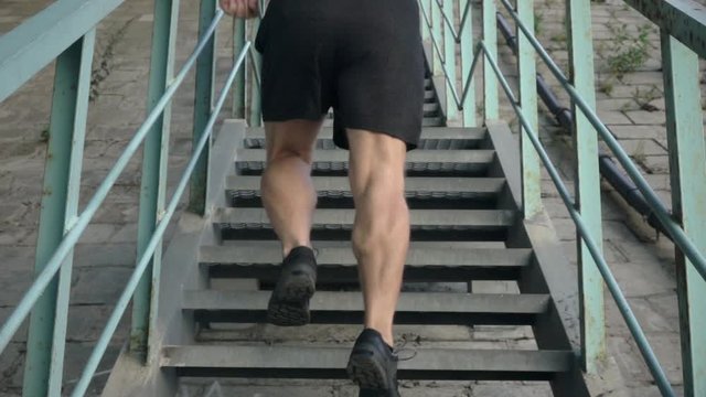 Active senior man doing exercises on iron stairs and running up. Rear view. Active leisure. Close up outdoor shot of male legs in slow motion.