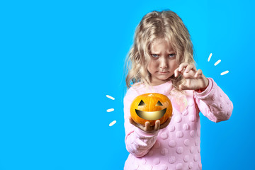 cute witch girl with blonde hair conjures over a pumpkin on colored background