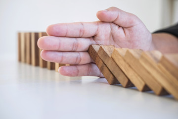 Risk and Strategy in Business, Image of hand stopping falling collapse wooden block dominoes effect from continuous toppled block, prevention and development to stability
