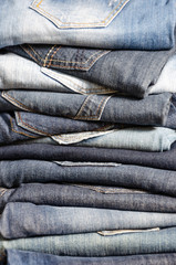 A stack of carelessly folded jeans on gray background. Close-up of jeans in different colors. Jeans...