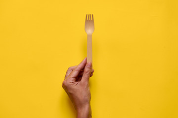 wood fork in woman hand in top view isolated on yellow background. minimal