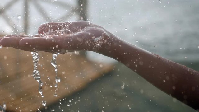 Water streams in the solar rays fall on the young woman's hands.