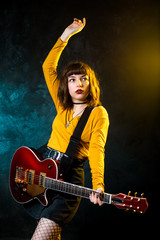 Portrait of beautiful young hipster woman with curly hair with red guitar in neon lights. Rock musician is playing electrical guitar. 90s style concept.