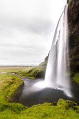 Icelandic landscape with the iconic waterfall of Seljalandsfoss under a cloudy sky