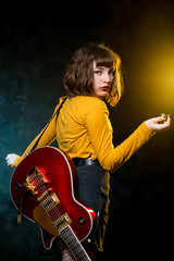 Portrait of beautiful young hipster woman with curly hair with red guitar in neon lights. Rock musician is playing electrical guitar. 90s style concept.