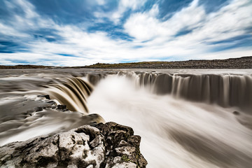 Icelandic landscape with a wide angle shot of Selfoss waterfall under a blue sky with clouds