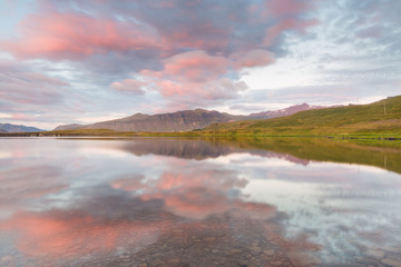Symmetrical shot of an icelandic landscape, with pink clouds and distant mountains reflecting on a still lake